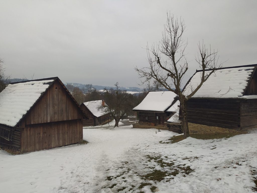 Záběr na shluk zasněžených chalup ve Valašské dědině v Rožnově pod Radhoštěm