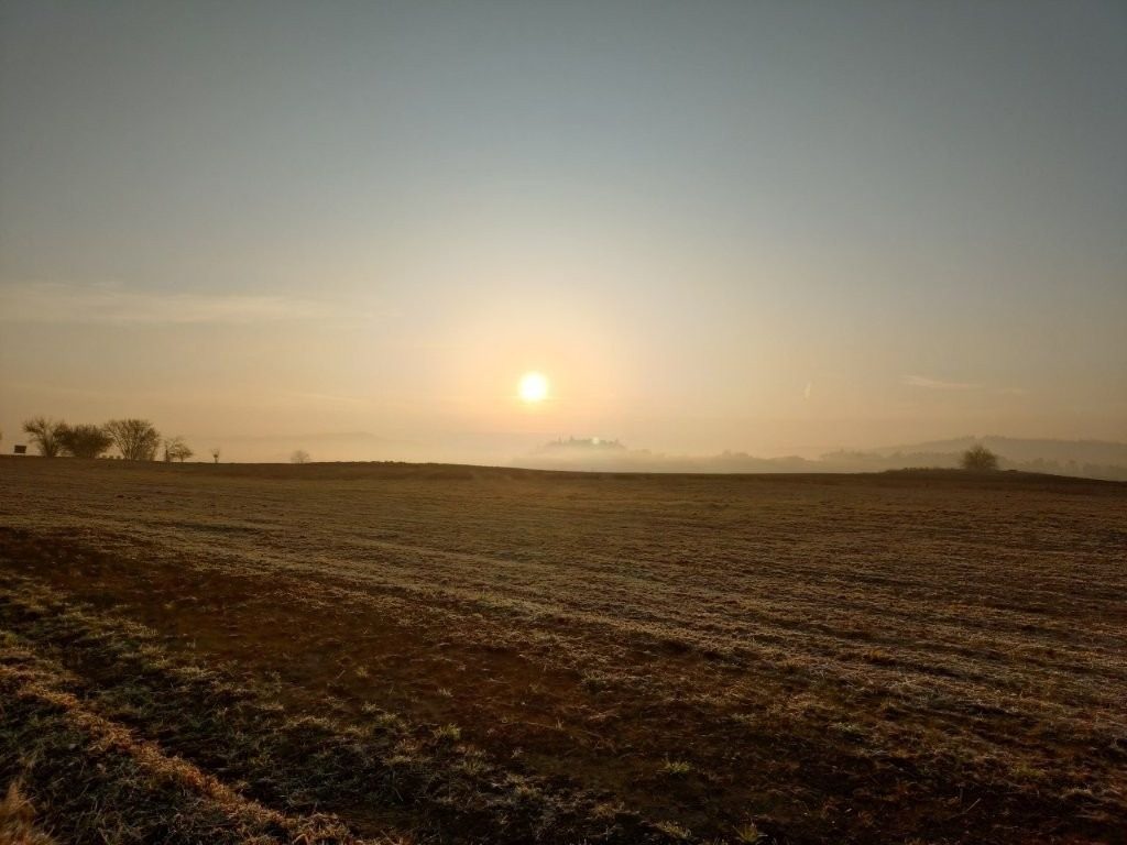 Jasně zářácí slunce na obzoru, které osvětluje pole